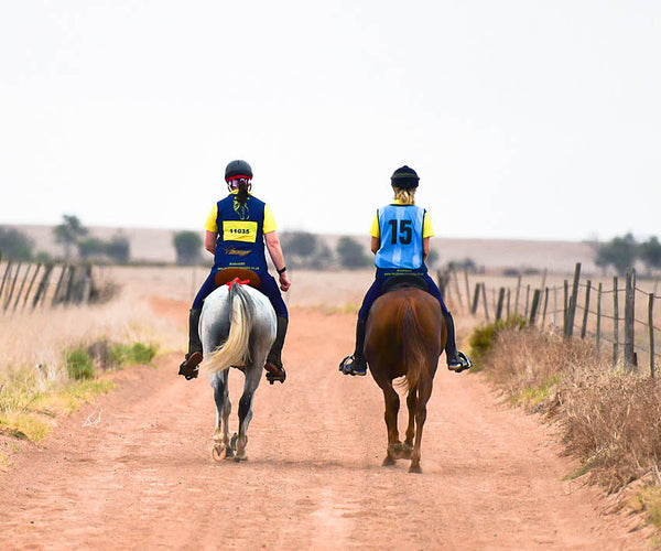 Riders riding down a dirt road in a riding competition in Scoot Boots